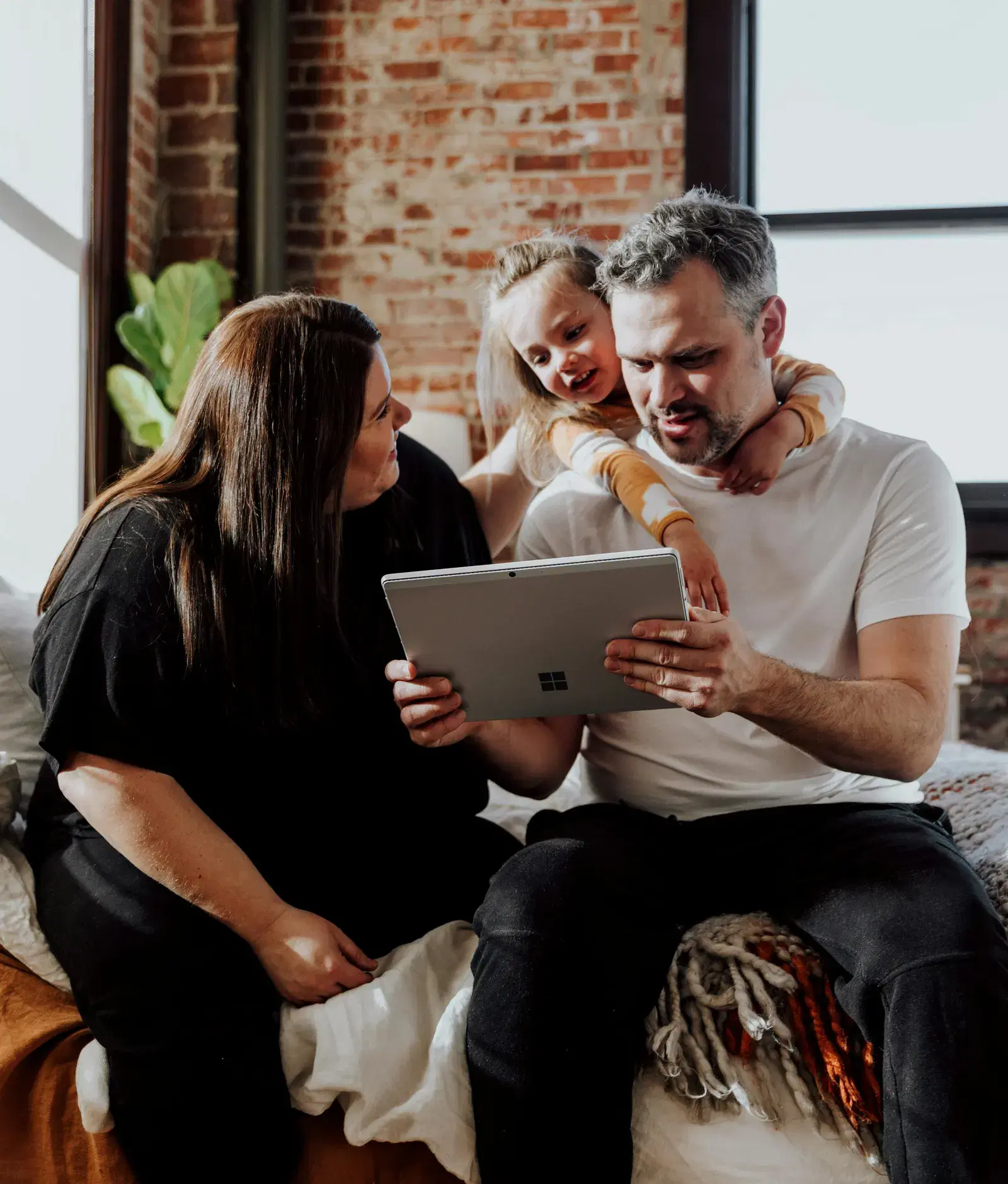 Two parents and a young child sitting together at home, looking at a tablet